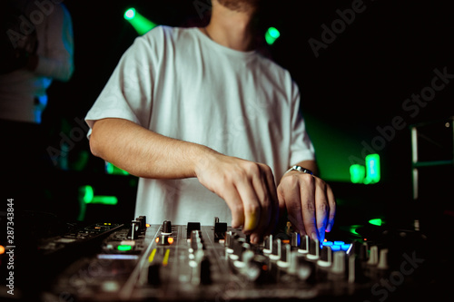 Close up view of the hands of a male disc jockey mixing music on his deck with his hands poised over the vinyl record on the turntable and the control switches at night © Семен Саливанчук