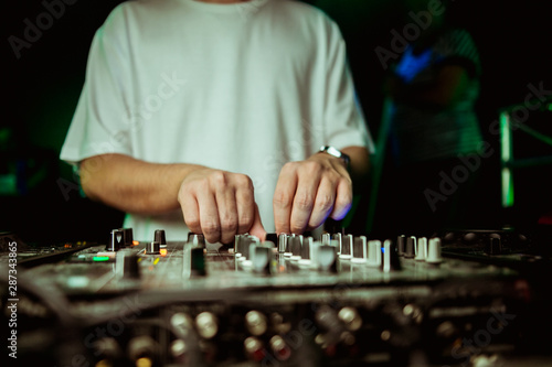 Close up view of the hands of a male disc jockey mixing music on his deck with his hands poised over the vinyl record on the turntable and the control switches at night © Семен Саливанчук