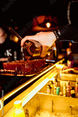 Barman pouring fresh alcoholic drink into the glasses with ice cubes on the bar counter