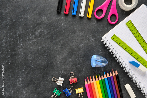 School supplies such as ruler, notebook, pens, pencils, scissors on chalkboard