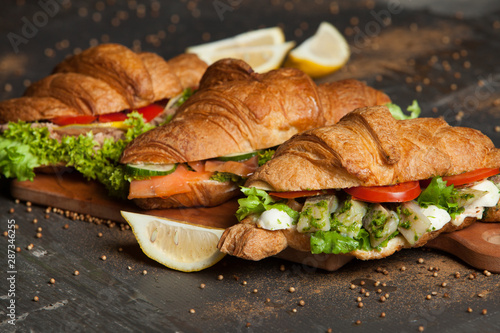 Croissant sandwiches served on wooden board. Croissants with egg, melted cheese, parsley, chicken ham, smoked salmon