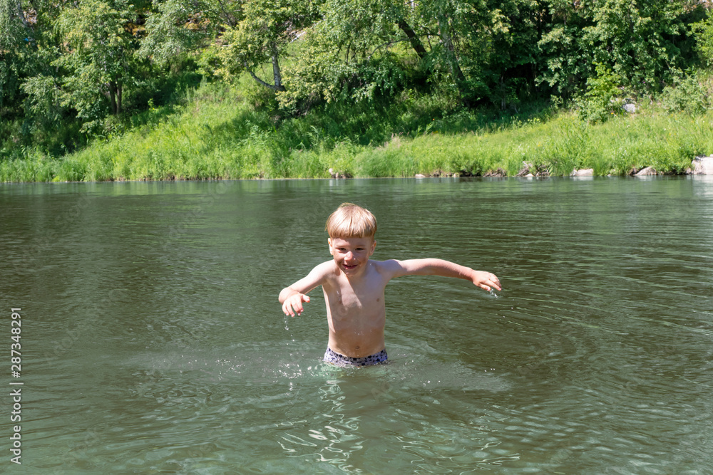 smiling 5 year old kid is happy to bathe in the sea or river. The child in the summer plays in the water. .green forest on the background