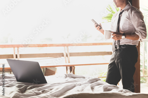 Laptop on the bed with businessman using cellphone and holding coffee in cup. photo