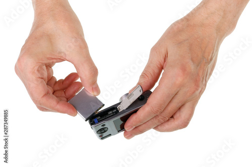 Elderly senior man inserts lithium rechargeable battery  into a conpact photo camera isolated