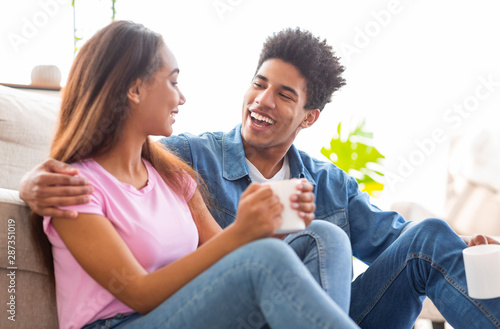 Teenage couple in love drinking coffee sitting on floor indoors.