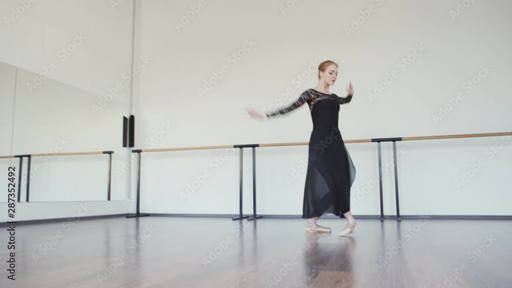 Tilt down wide shot of graceful ballerina in pointe shoes, black lace leotard and long wrap skirt rehearsing alone in dance studio with mirrors and barre at walls Tilt down wide shot of graceful ballerina in pointe shoes, black lace leotard and long wrap skirt rehearsing alone in dance studio with mirrors and barre at walls