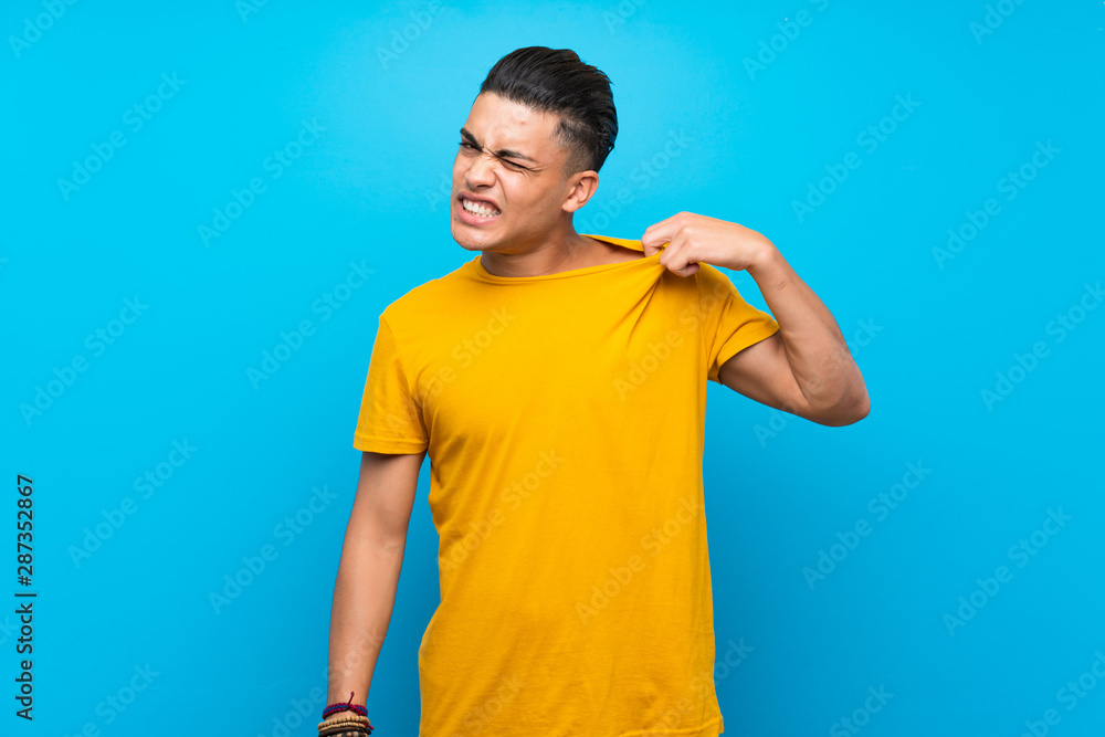 Young man with yellow shirt over isolated blue background with tired and sick expression Young man with yellow shirt over isolated blue background with tired and sick expression