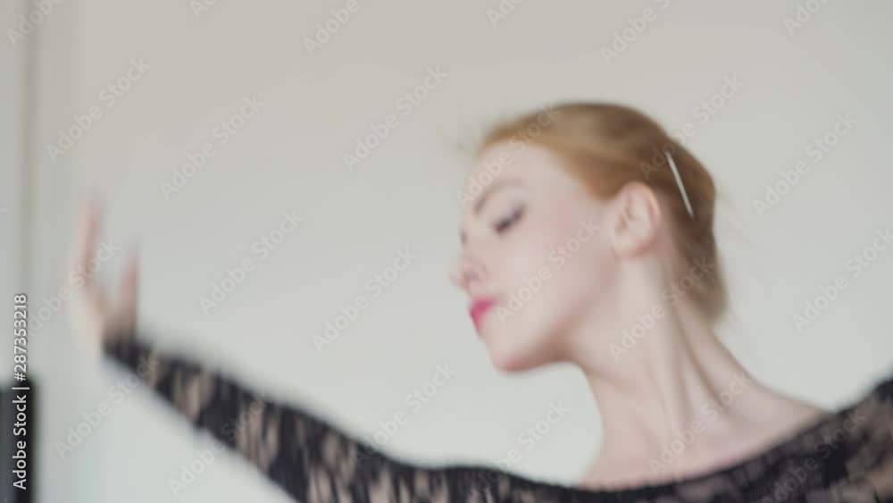 Zoom in of graceful redhead ballerina in black lace leotard rehearsing dance in ballet studio, closeup head and shoulders shot Zoom in of graceful redhead ballerina in black lace leotard rehearsing dance in ballet studio, closeup head and shoulders shot