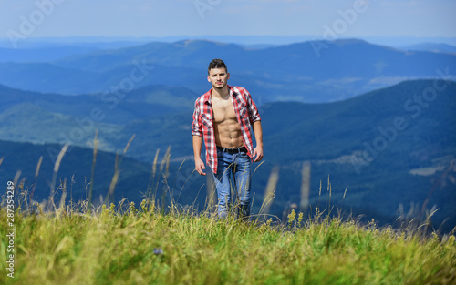 Hiking concept. Man stand top mountain landscape background. Muscular tourist walk mountain hill. Hiker muscular torso reach mountain peak. Athlete guy relax mountains. Beautiful environment
