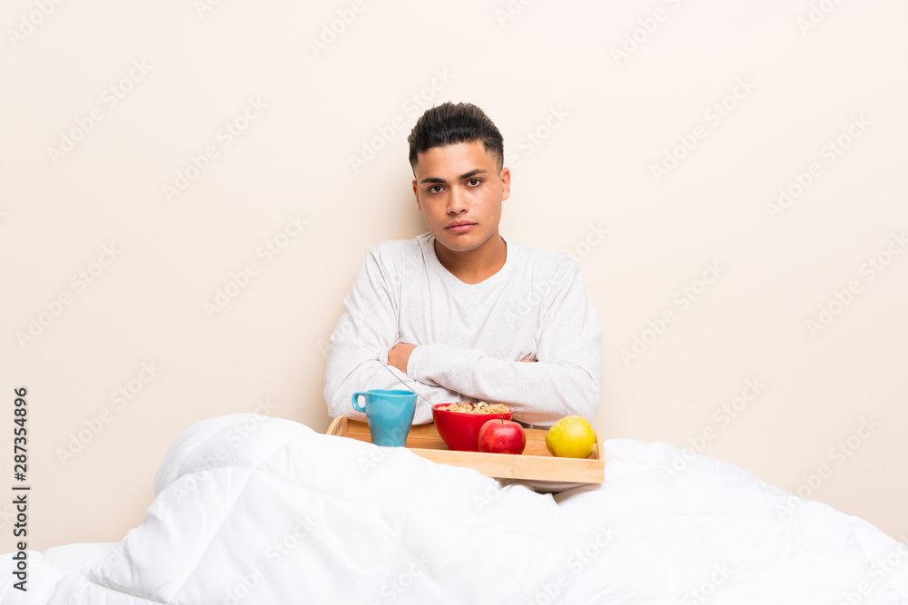 Young man having breakfast in bed keeping arms crossed Young man having breakfast in bed keeping arms crossed