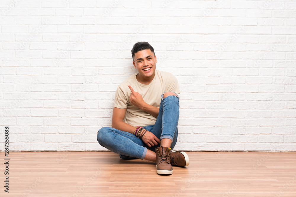Young man sitting on the floor pointing finger to the side Young man sitting on the floor pointing finger to the side