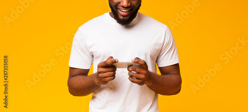 Excited african american guy using smartphone on yellow background