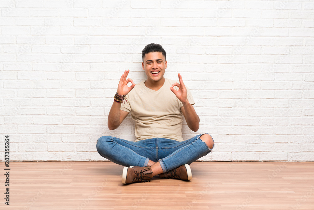 Young man sitting on the floor showing an ok sign with fingers Young man sitting on the floor showing an ok sign with fingers