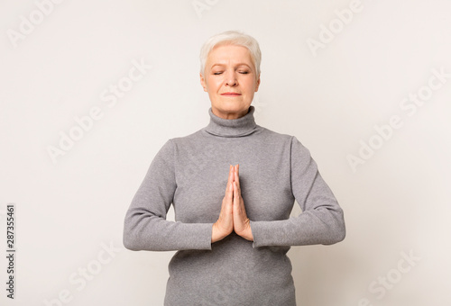 Elderly woman meditating indoors showing namaste gesture © Prostock-studio