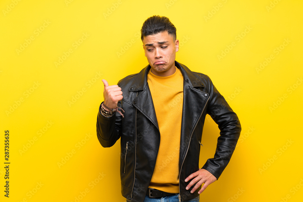Young man over isolated yellow background unhappy and pointing to the side Young man over isolated yellow background unhappy and pointing to the side