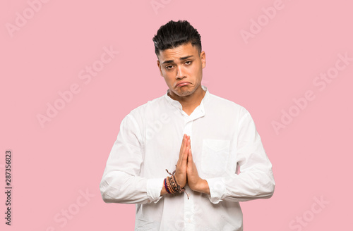 Young man keeps palm together. Person asks for something on colorful background