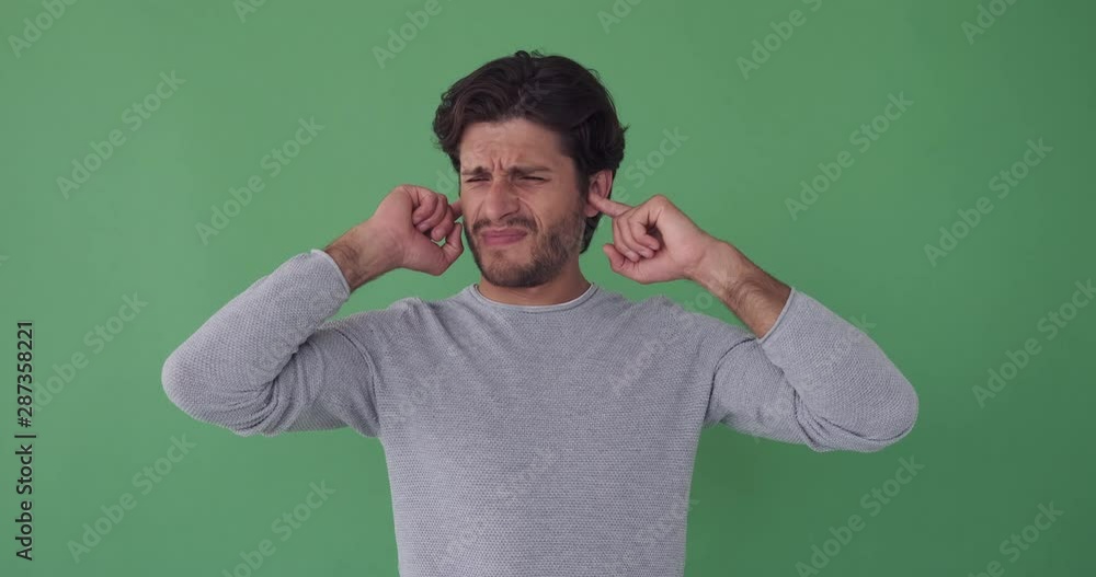 Unhappy man closing his ears with fingers and gesturing no over green background Unhappy man closing his ears with fingers and gesturing no over green background