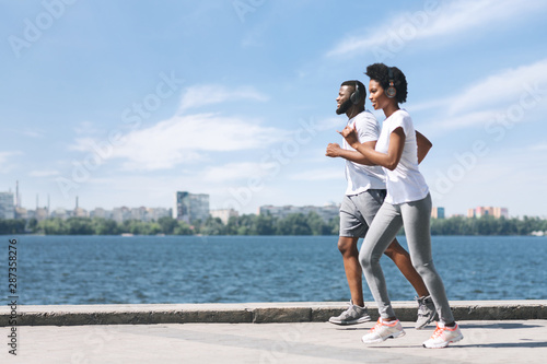 Fototapeta Naklejka Na Ścianę i Meble -  Sporty Black Couple Jogging Along River Embankment Outdoor