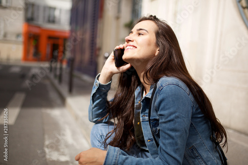 Side of happy young woman sitting on street talking with cellphone © mimagephotos