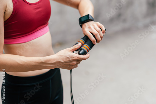 Cropped portrait of fit young woman in sportswear holding jump rope in city park. Horizontal shot