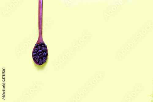 Coffee beans in a wooden spoon on a yellow background