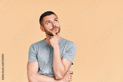 Young thoughtful man thinking and looking aside on copy space isolated on yellow background photo