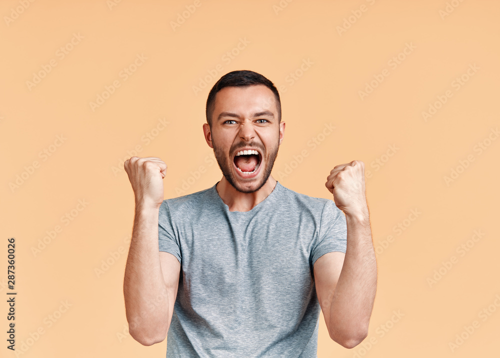 © GVS - Happy man celebrating his success with winner gesture on beige background