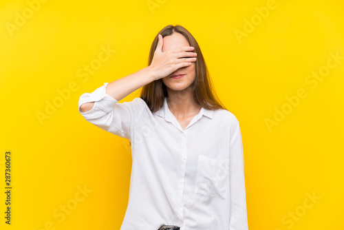 Young woman over isolated yellow background covering eyes by hands © luismolinero
