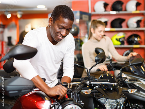 Portrait of young man buying new motorcycle at modern showroom