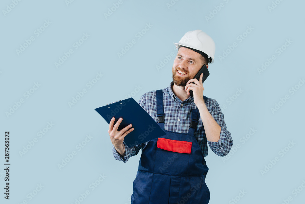 Happy construction worker in a white helmet and blue overalls with a phone Happy construction worker in a white helmet and blue overalls with a phone