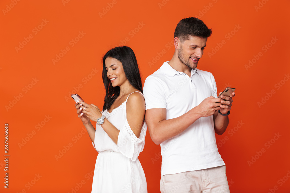 Young amazing loving couple posing isolated over red wall background using mobile phones.