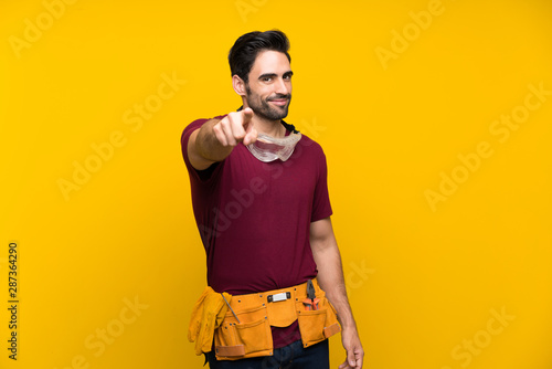 Handsome young craftsman over isolated yellow background points finger at you with a confident expression photo