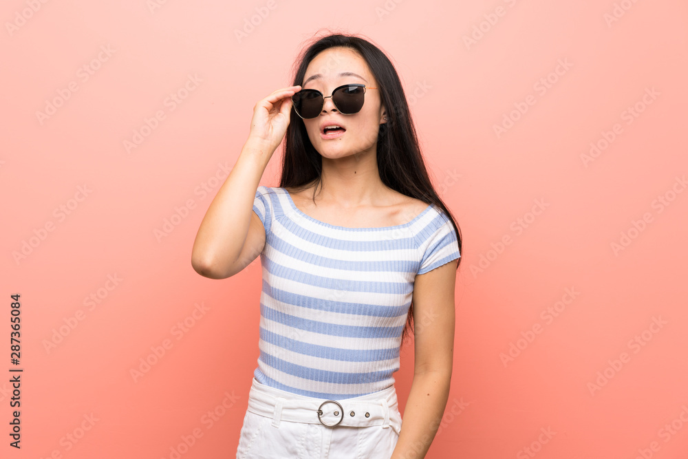 Teenager asian girl over isolated pink background with glasses and surprised Teenager asian girl over isolated pink background with glasses and surprised