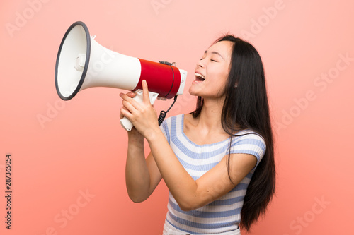 Teenager asian girl over isolated pink background shouting through a megaphone