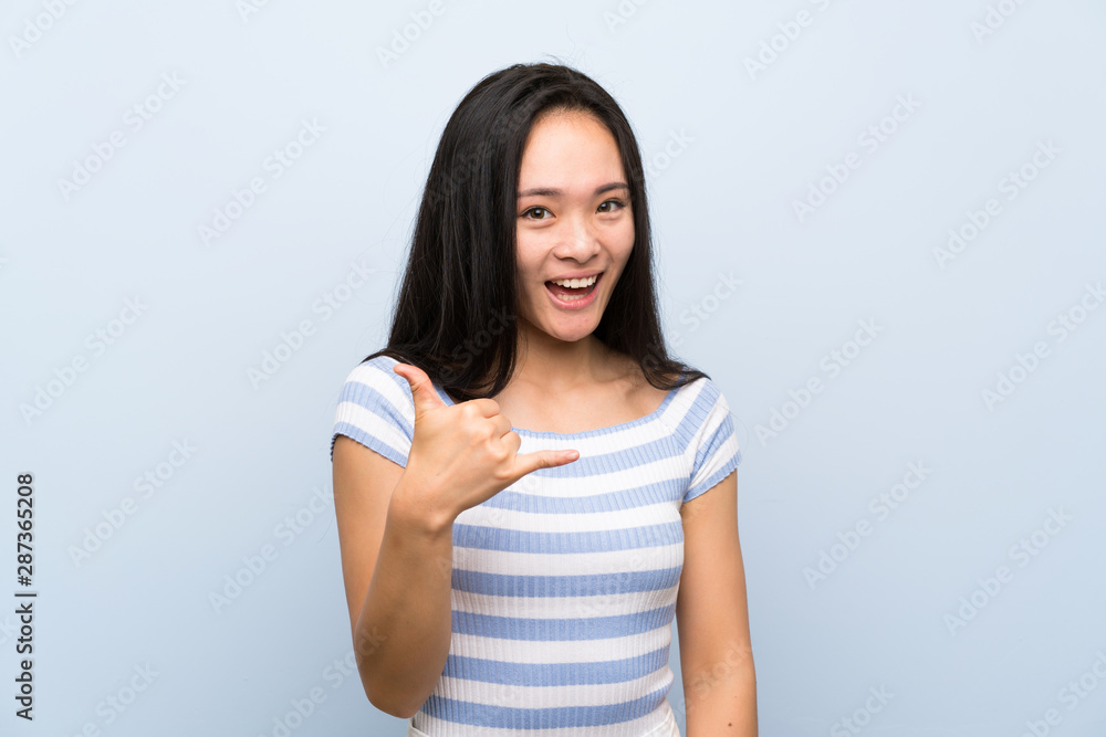 Teenager asian girl over isolated blue background making phone gesture Teenager asian girl over isolated blue background making phone gesture
