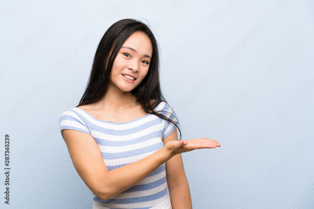 Teenager asian girl over isolated blue background extending hands to the side for inviting to come - obrazy, fototapety, plakaty 