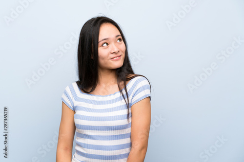 Teenager asian girl over isolated blue background laughing and looking up