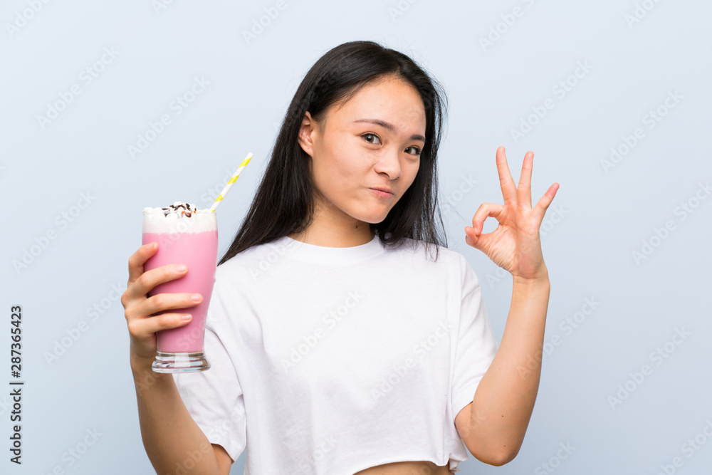 Teenager asian girl holding a strawberry milkshake showing ok sign with fingers Teenager asian girl holding a strawberry milkshake showing ok sign with fingers