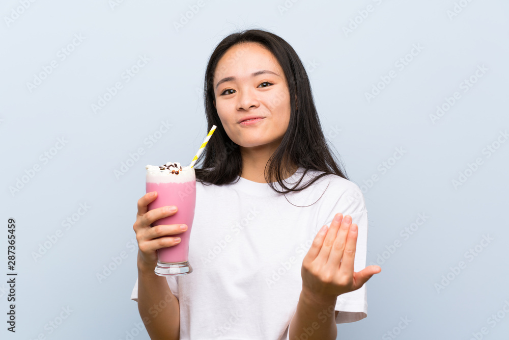 Teenager asian girl holding a strawberry milkshake inviting to come with hand. Happy that you came Teenager asian girl holding a strawberry milkshake inviting to come with hand. Happy that you came