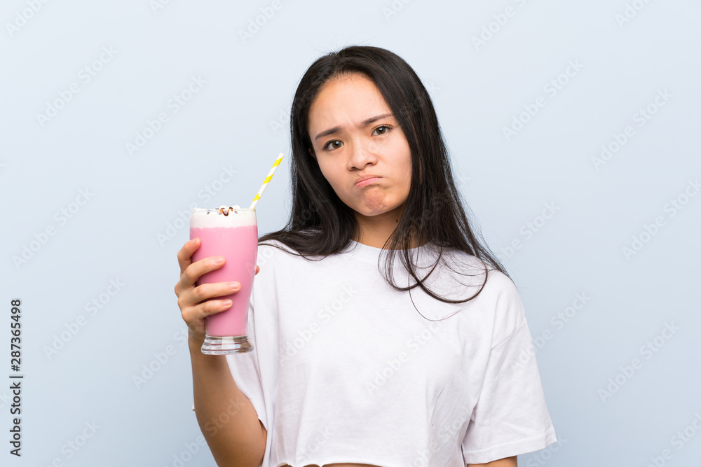 Teenager asian girl holding a strawberry milkshake with sad expression Teenager asian girl holding a strawberry milkshake with sad expression