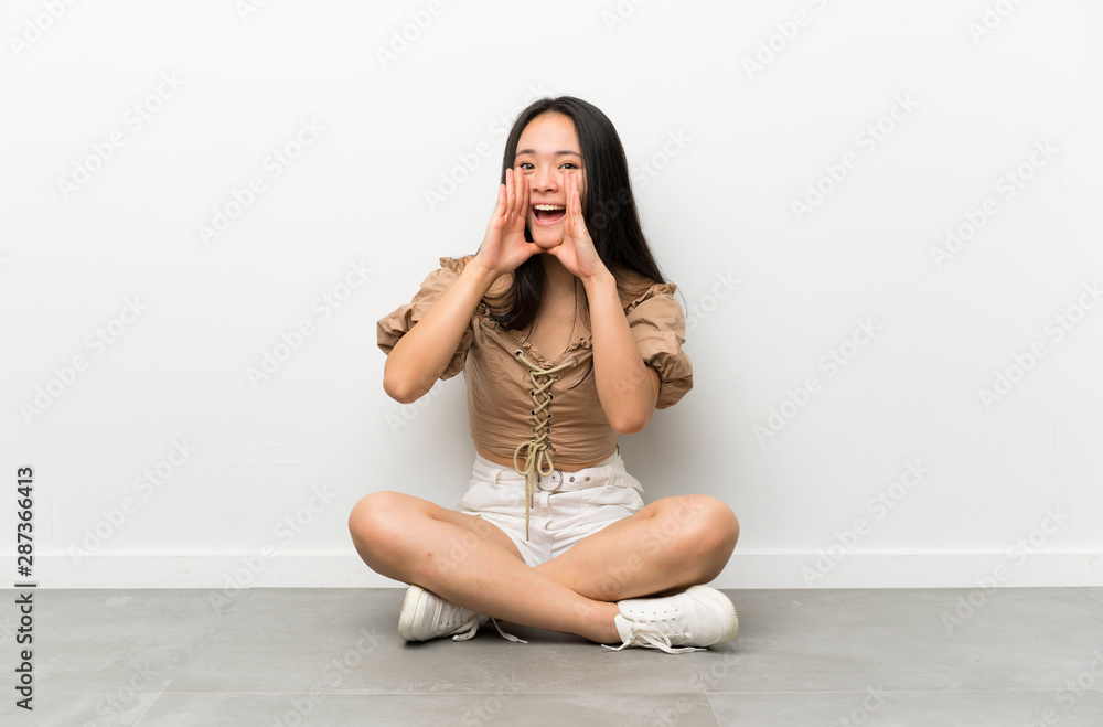 Teenager asian girl sitting on the floor shouting with mouth wide open Teenager asian girl sitting on the floor shouting with mouth wide open