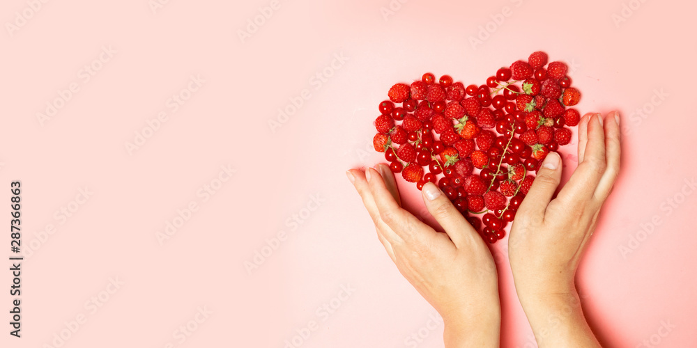 Female hands and red berries in the shape of a heart on a pink background. Female hands and red berries in the shape of a heart on a pink background.