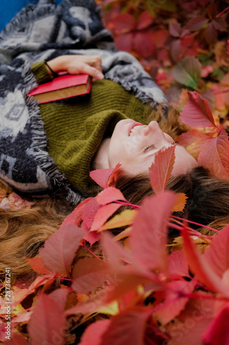 Girl lying among colorful ivy foliage in autumn and holding a paper book with red cover