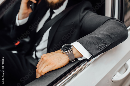 Close up of expensive watch on a man sitting at the wheel of a white car.