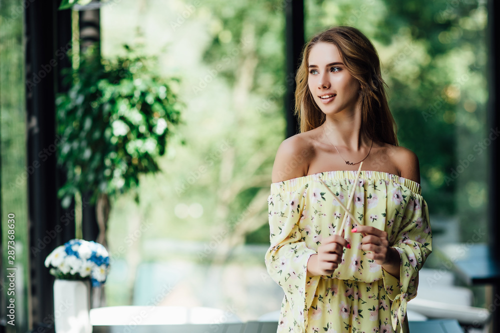 Gorgeous woman holding sushi chopsticks while looking forward to at modern cafe terrace. Gorgeous woman holding sushi chopsticks while looking forward to at modern cafe terrace.