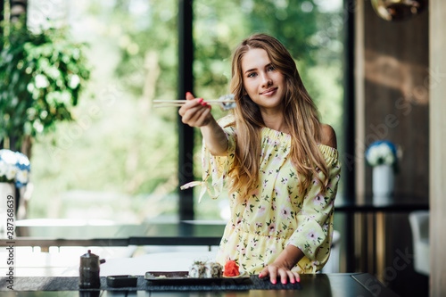 Attractive, blonde girl in chinese restaurant with sushi rolls posing and smiling.