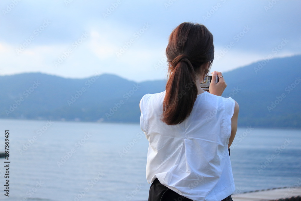 A woman is taking a photo in front of beautiful lake. A woman is taking a photo in front of beautiful lake.
