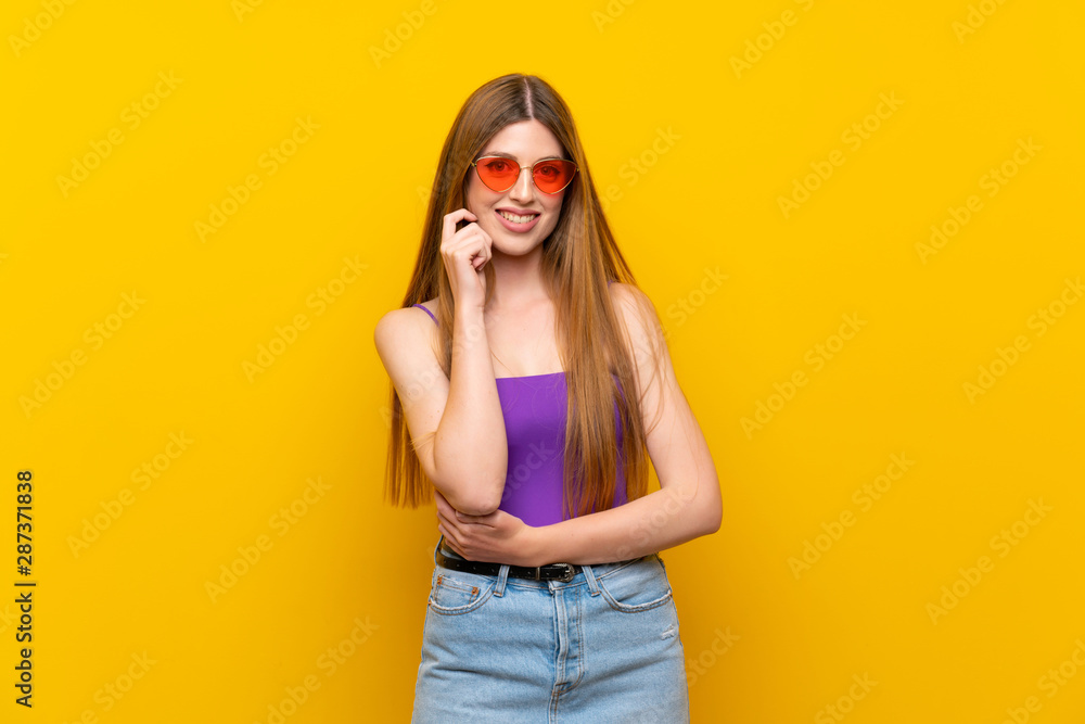 Young woman over isolated yellow background with glasses and smiling