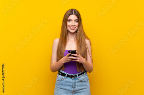 Young woman over isolated yellow background sending a message with the mobile
