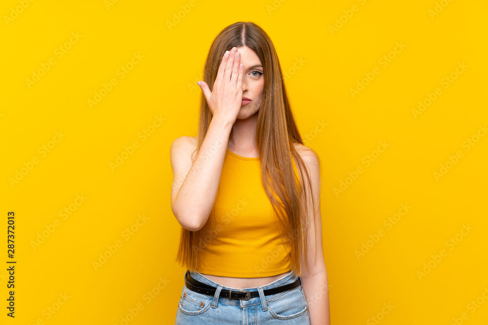 Fototapeta premium Young woman over isolated yellow background covering a eye by hand